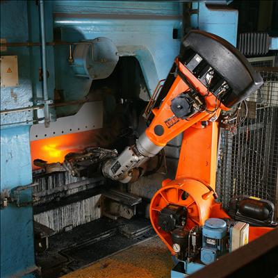 An orange industrial robot arm working at a foundry furnace