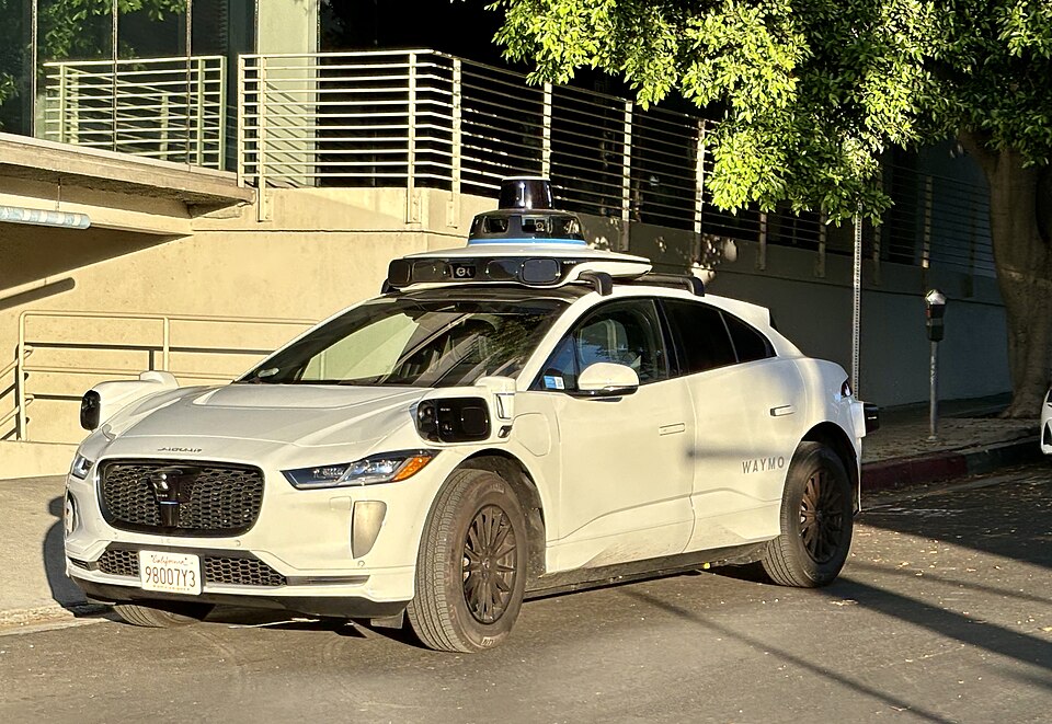 A white Waymo self-driving Jaguar with sensors on its roof, parked on a street
